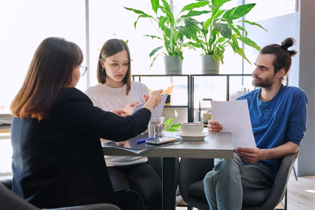 Couple of young clients at meeting with agent insurer realtor, reading paper contract