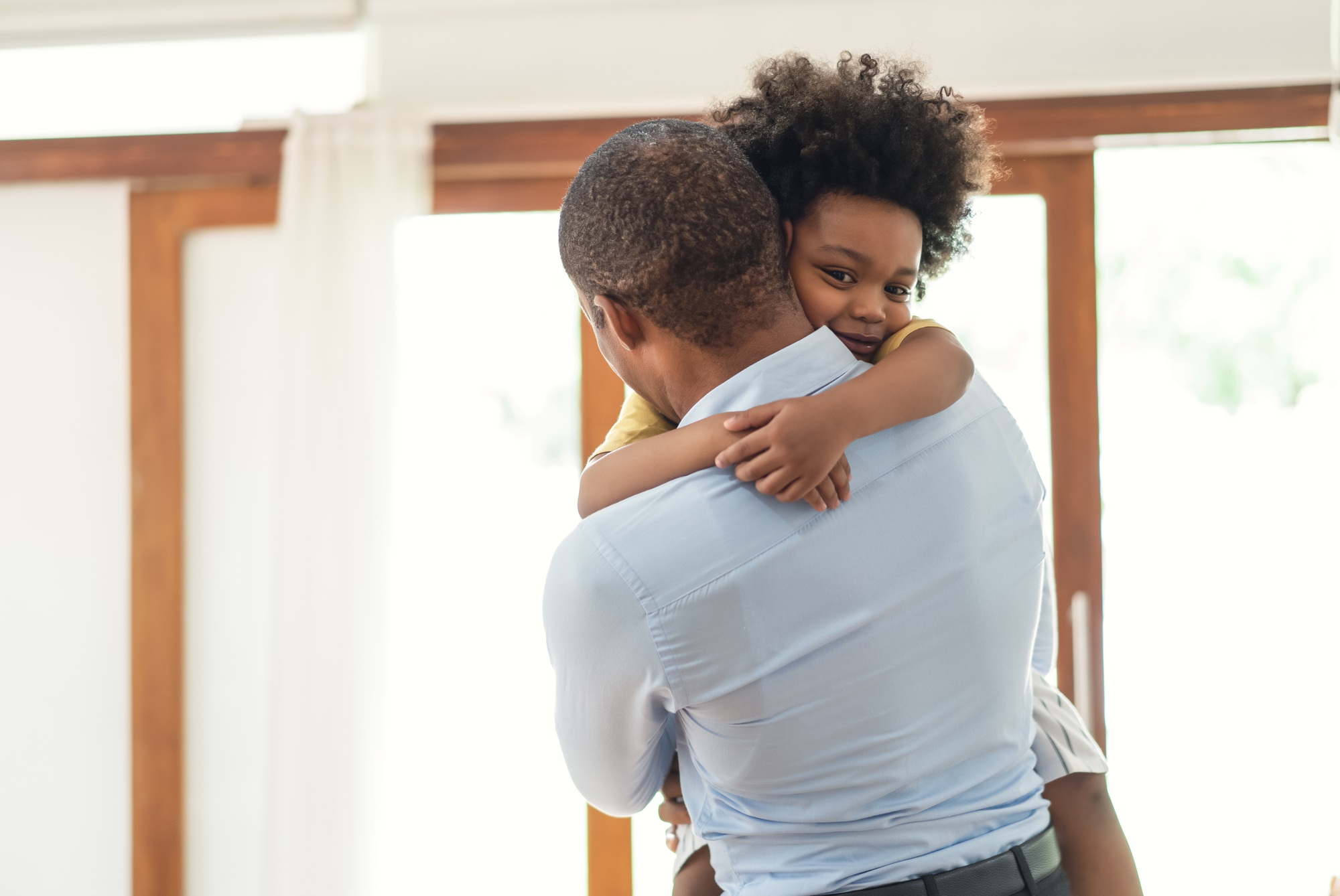 Loving African American father holding carrying adorable little son in living room